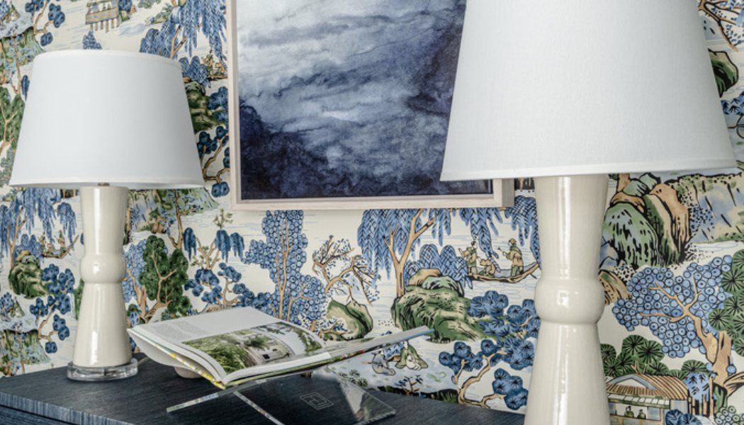Console table with ivory lamps and an abstract seascape against blue chinoiserie wallpaper
