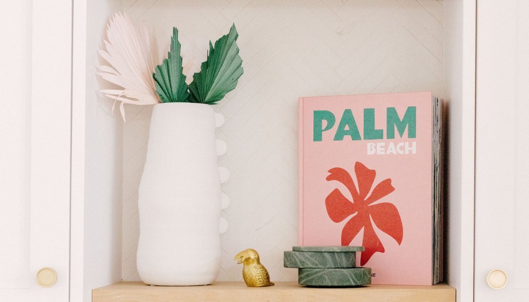 Styled built-in shelf with a white ribbed vase, palm fronds, marble coasters and a coffee-table book