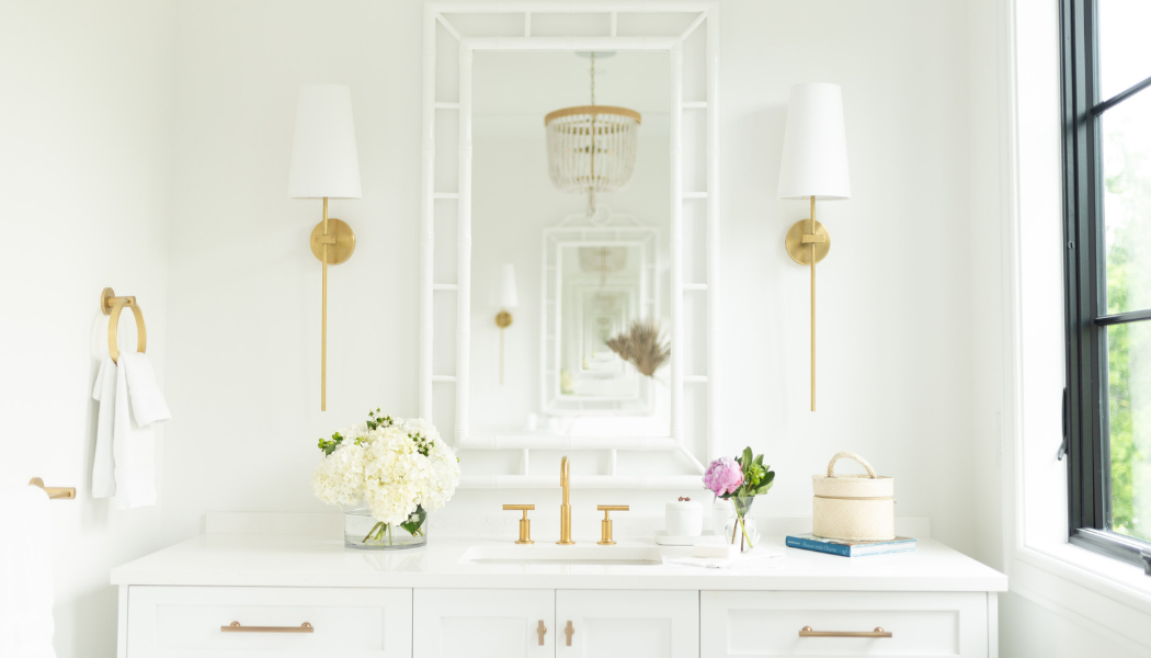 White bath vanity with brass sconces, a fretwork mirror and hydrangeas