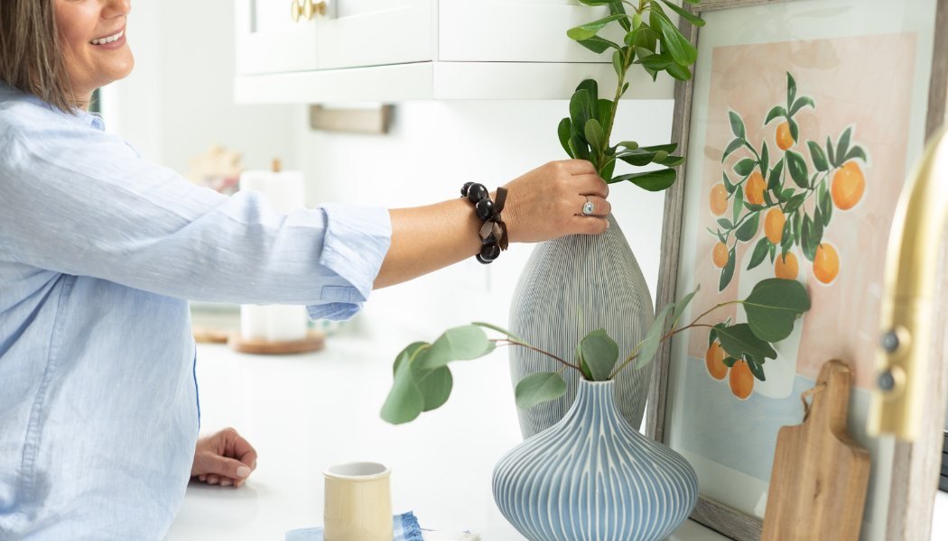 Andrea Dussault arranging greenery in a fluted vase on a kitchen counter