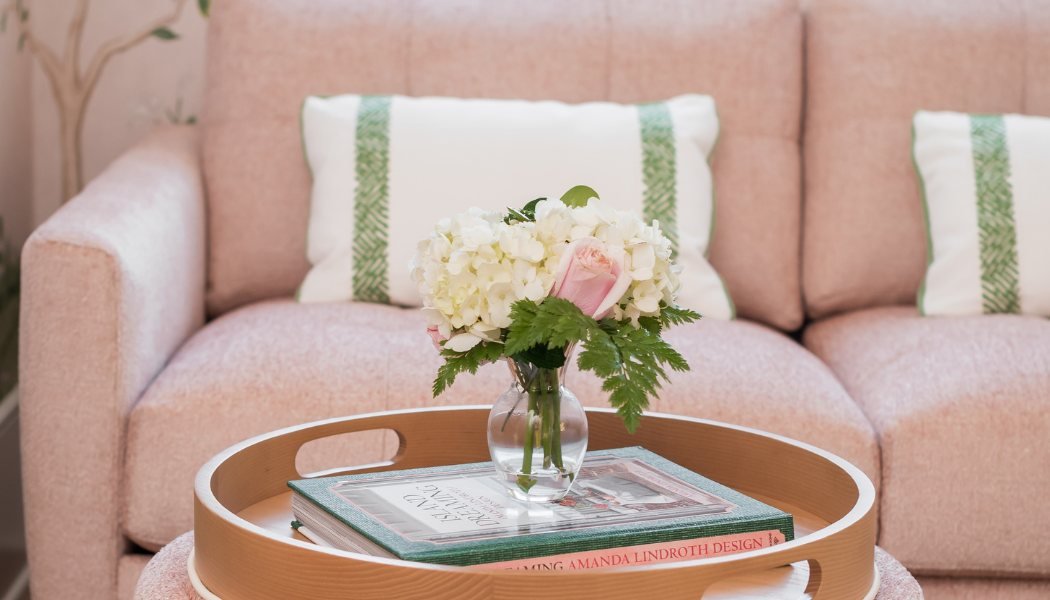 Blush sofa with green-striped pillows and a wood tray holding hydrangeas and design books