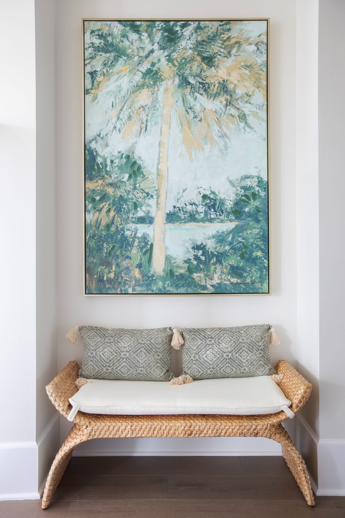 A framed palm painting hung above a woven bench with patterned lumbar pillows and a tailored cushion