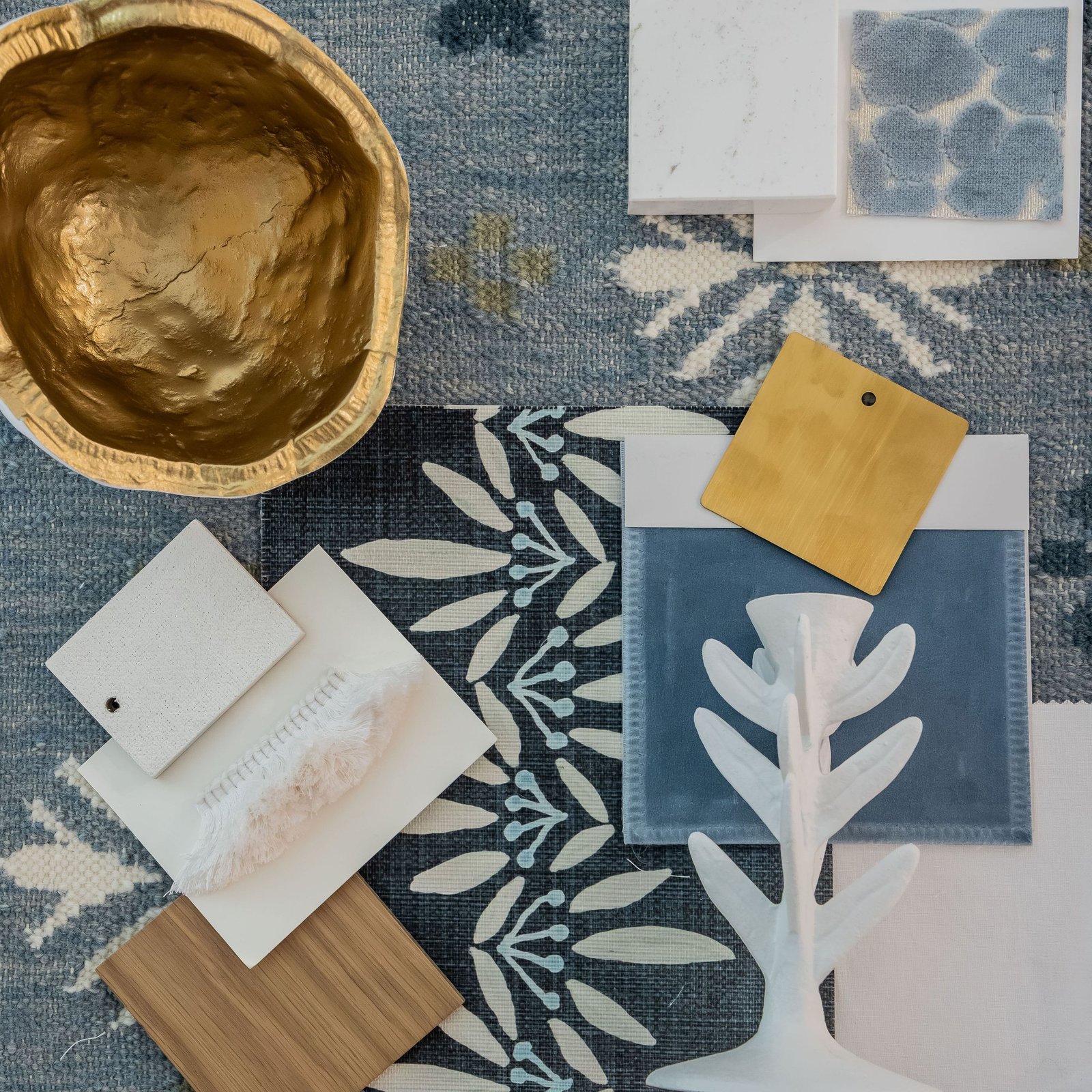 Flat lay of blue and cream fabric swatches, brass and stone samples on a woven rug