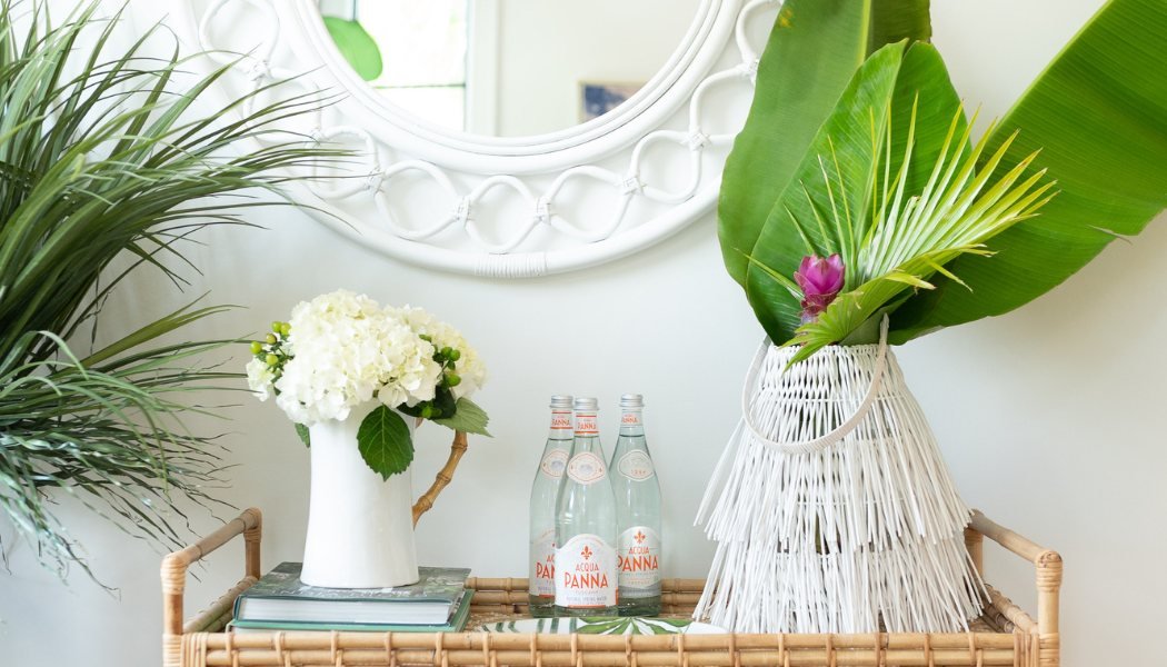 Rattan bar cart styled with white hydrangeas, palm fronds and a woven lantern beneath a round mirror