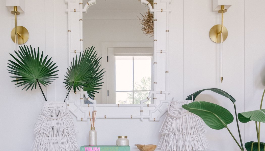 White entry vanity with a fretwork mirror, brass sconces, palm fronds and fringed lamps