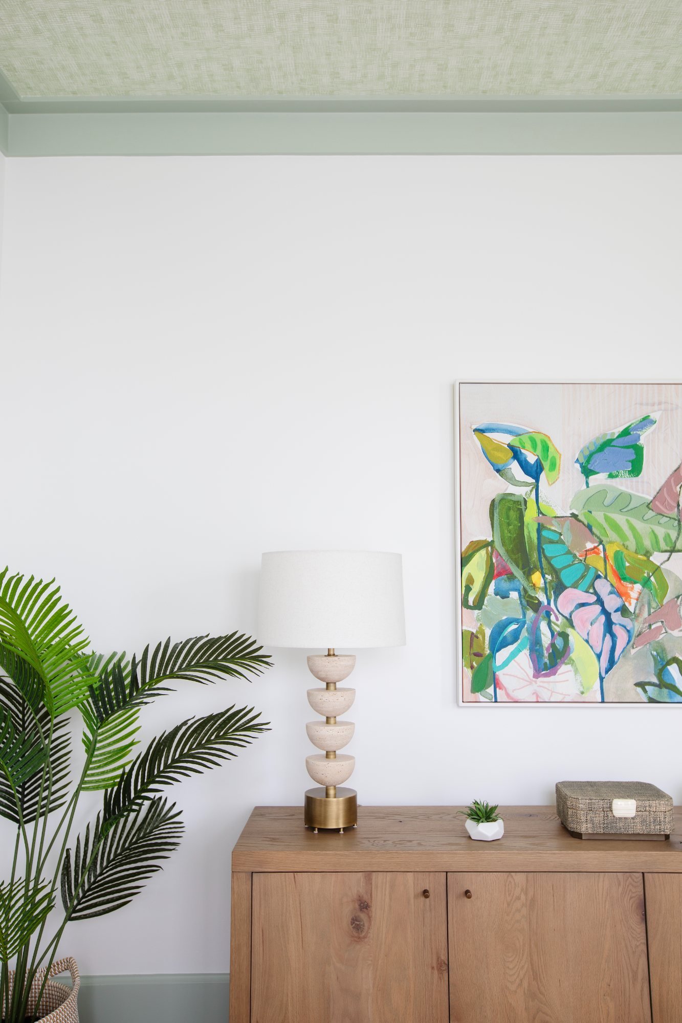 Travertine stacked lamp on a white oak credenza beneath a botanical canvas