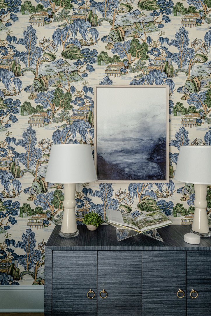 Navy grasscloth console with paired ivory lamps and a moody abstract canvas
