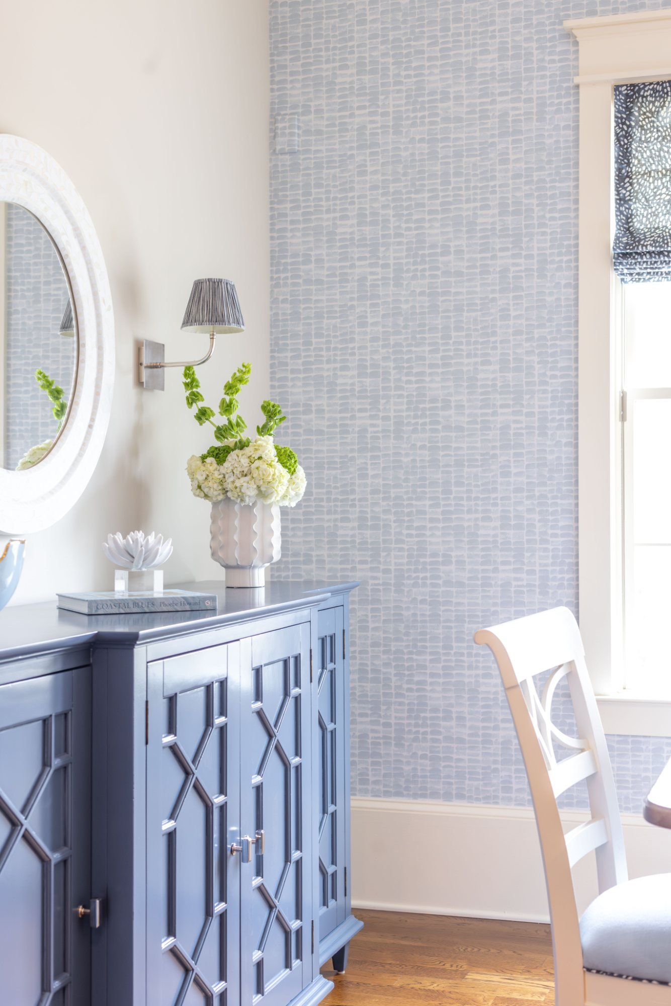 Blue fretwork sideboard with capiz mirror, pleated sconce, and hydrangeas