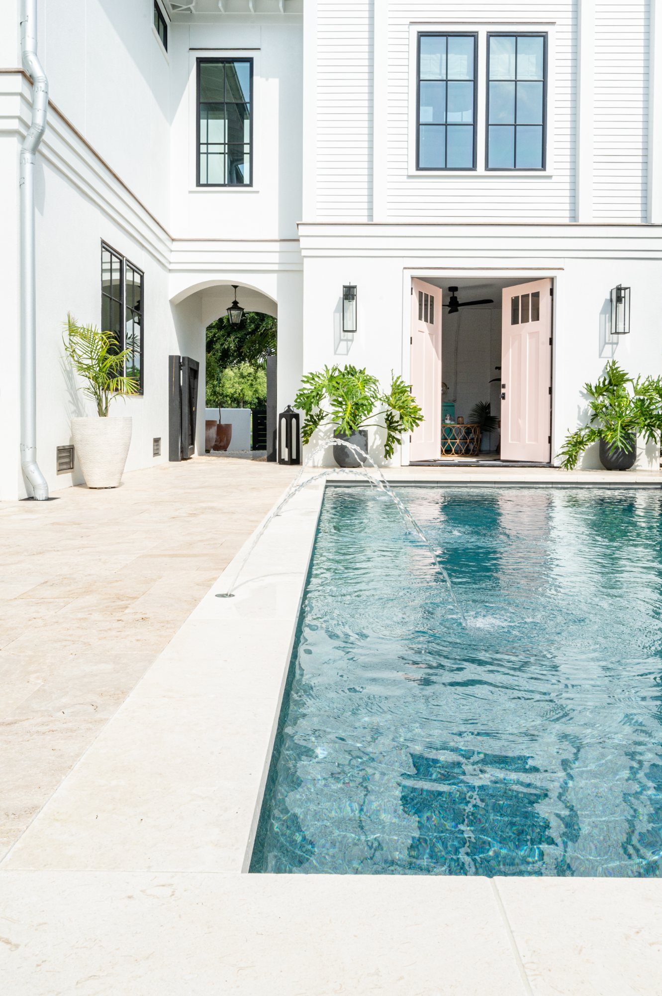 Pool with deck jets, pink doors, and lantern-lined loggia