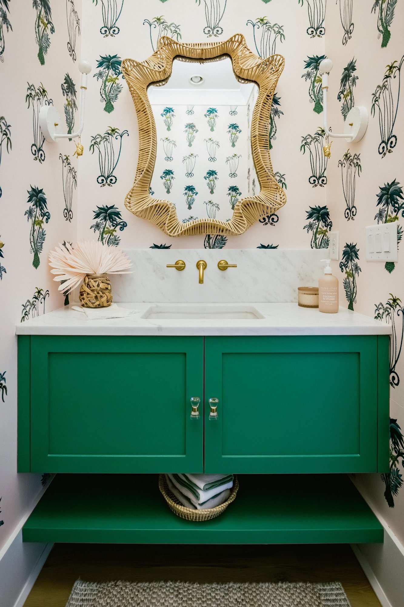 Powder room with emerald vanity, wavy rattan mirror, and palm wallpaper