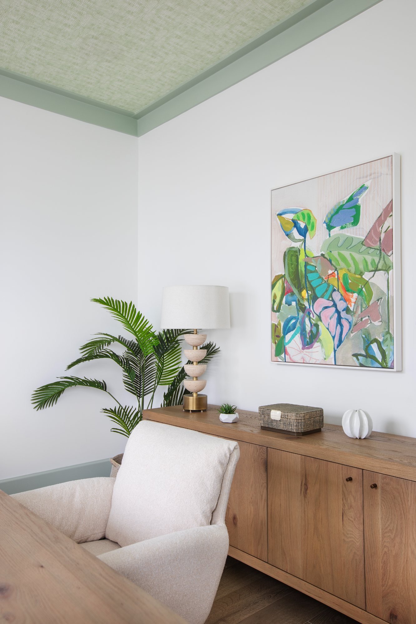 Study corner with palm, stacked travertine lamp, and framed botanical canvas