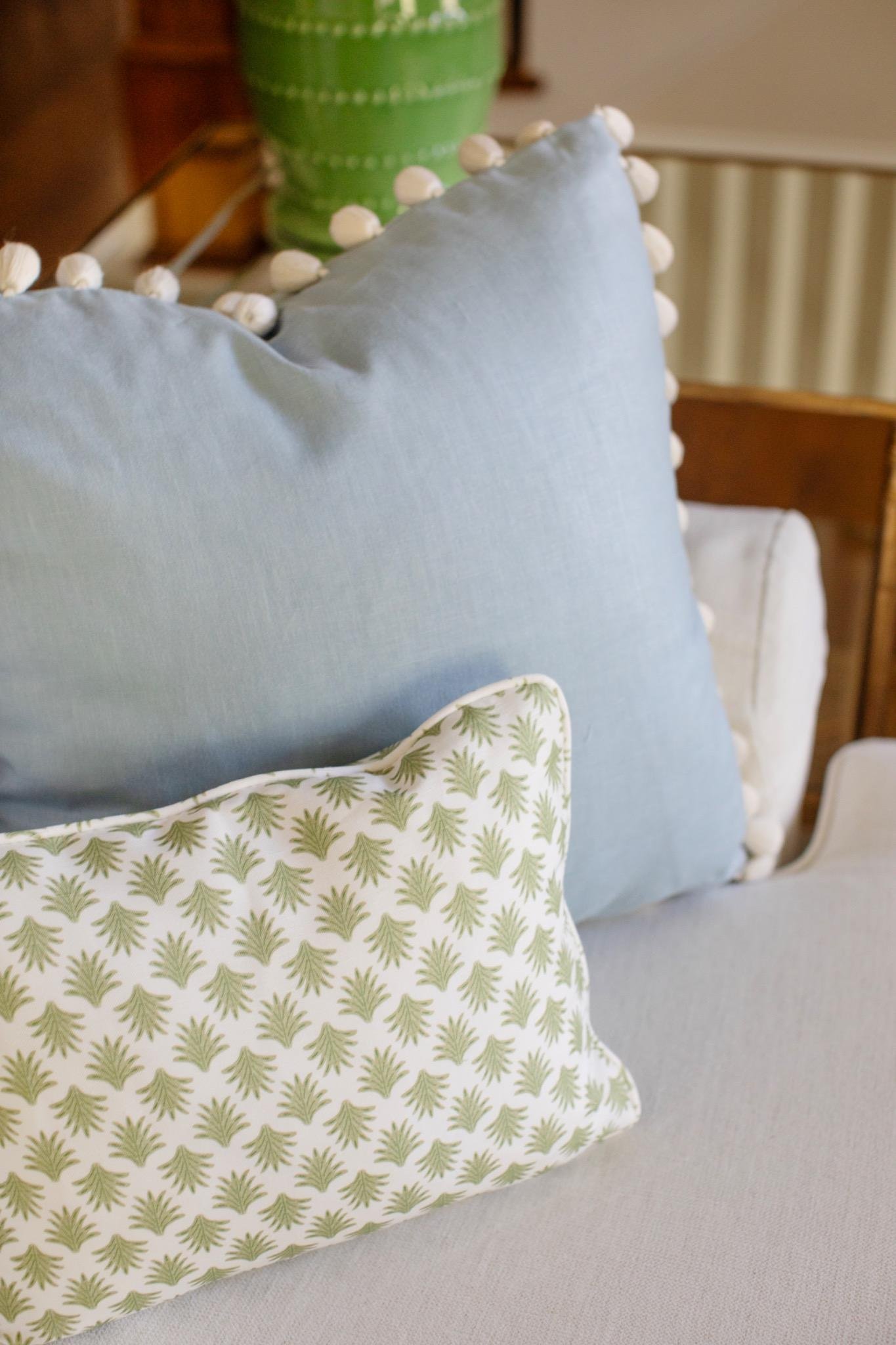 Blue linen pillow with pom-pom trim beside a green block-print lumbar pillow