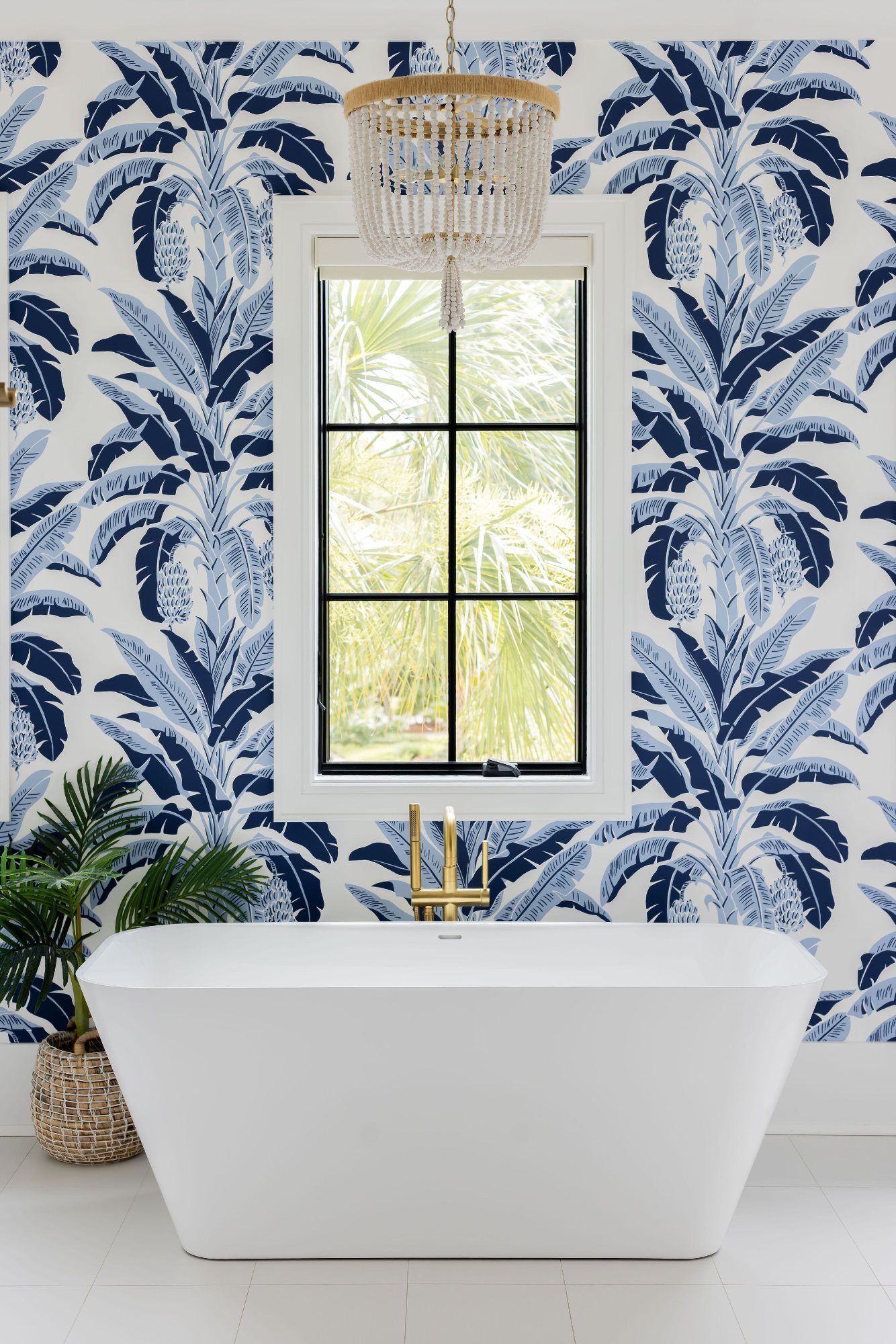 Freestanding tub against navy banana-leaf wallpaper with beaded chandelier