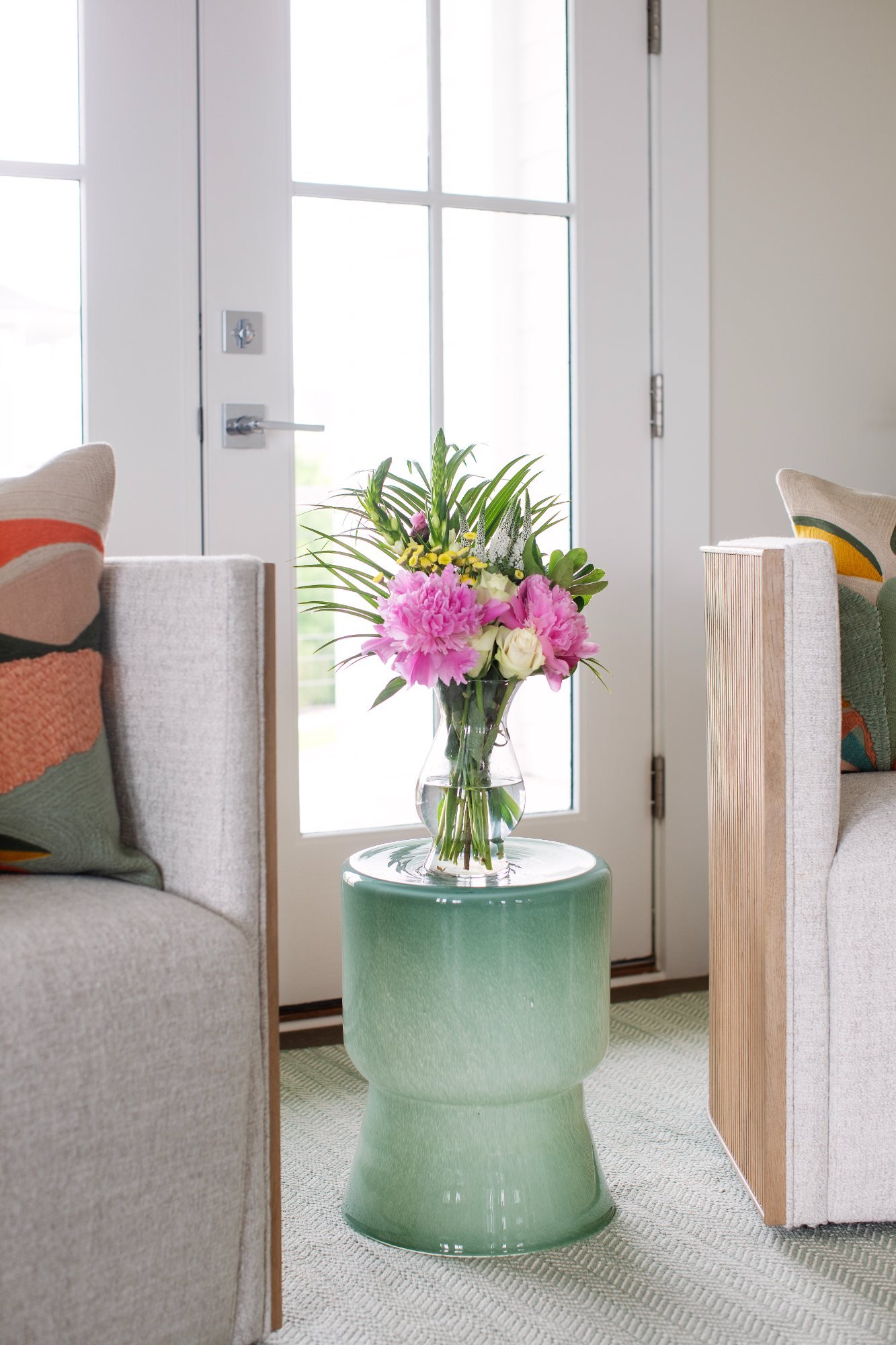 Peonies on a seafoam glass drink table between two upholstered chairs