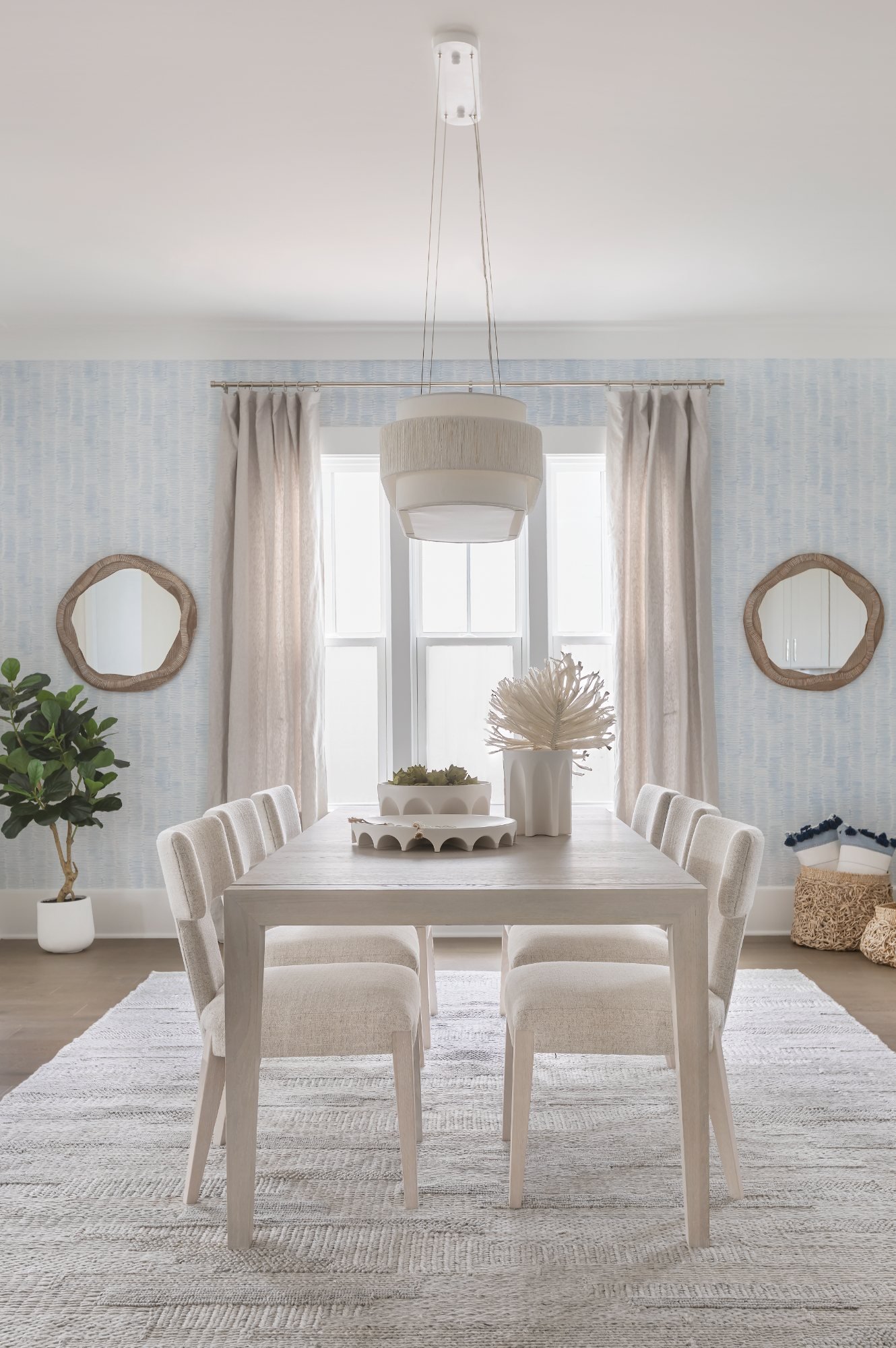 Dining room with fringed drum pendant, cerused table, and paired rattan mirrors