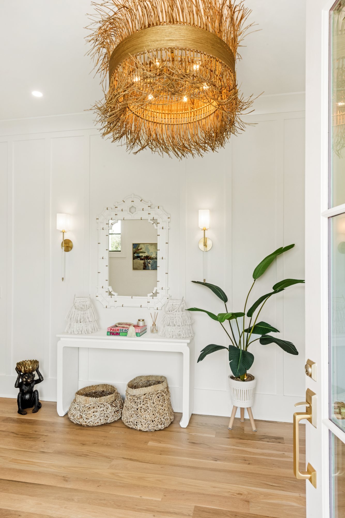 Entry with raffia fringe chandelier, white console, and bamboo mirror