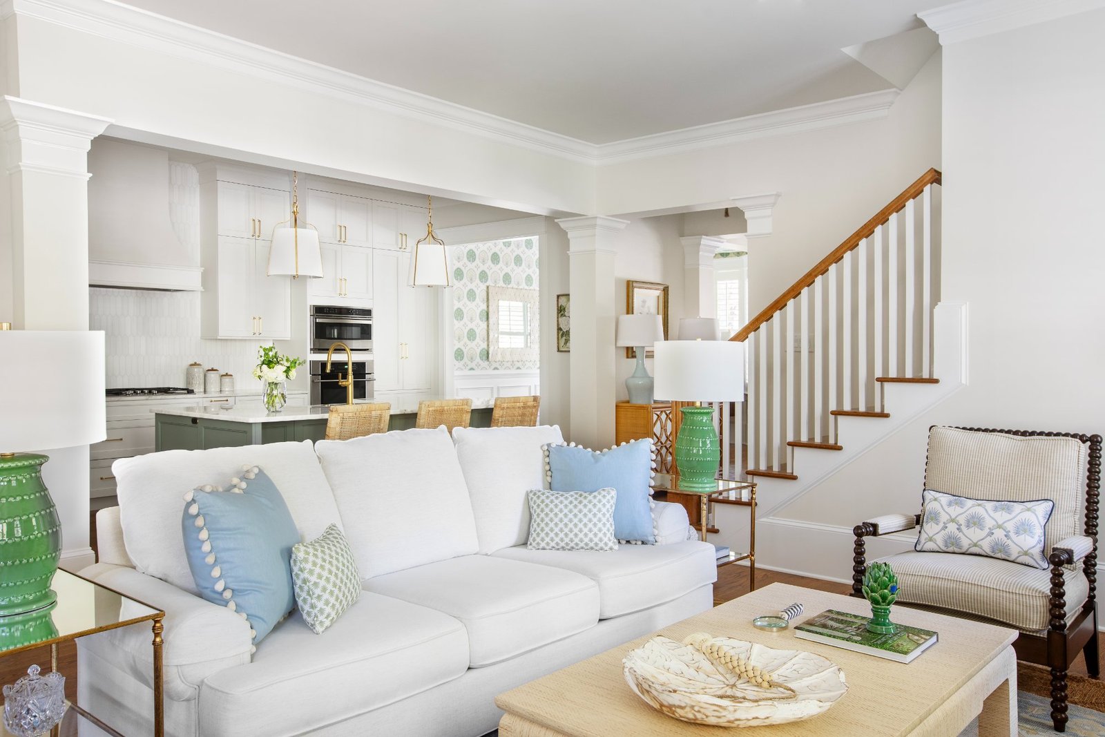 Living room with white slipcovered sofa, green ginger jar lamps, open to the kitchen and stair