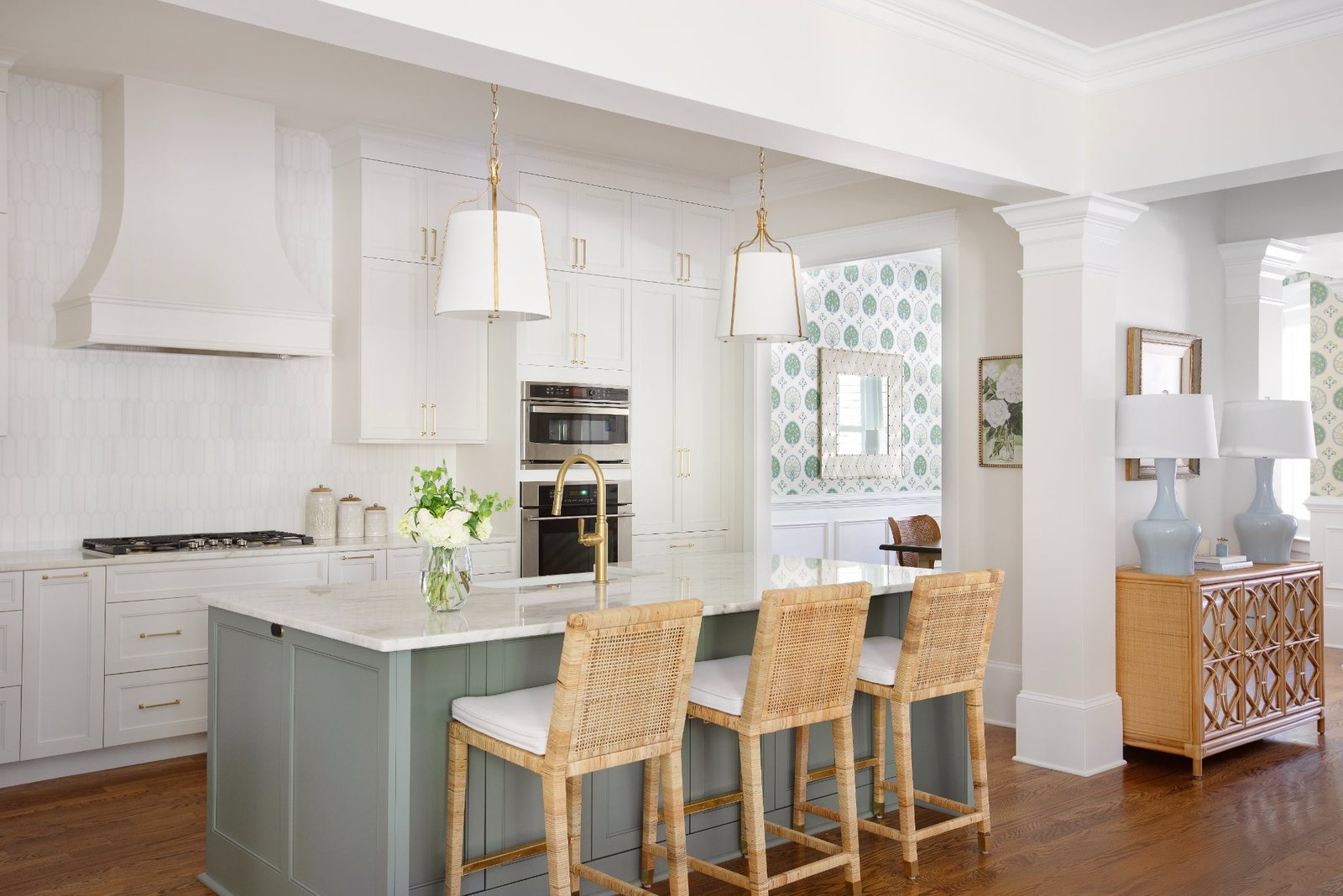 Kitchen with sage island, marble counters, brass pendants, and rattan counter stools