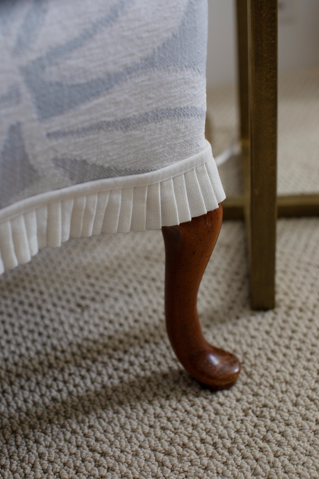 Pleated skirt and carved cabriole leg of the wing chair on looped wool carpet