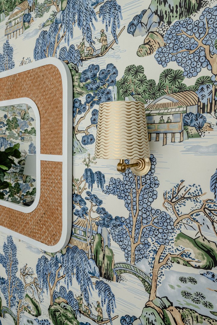 Brass sconce with wave-patterned shade beside a rattan mirror on chinoiserie paper