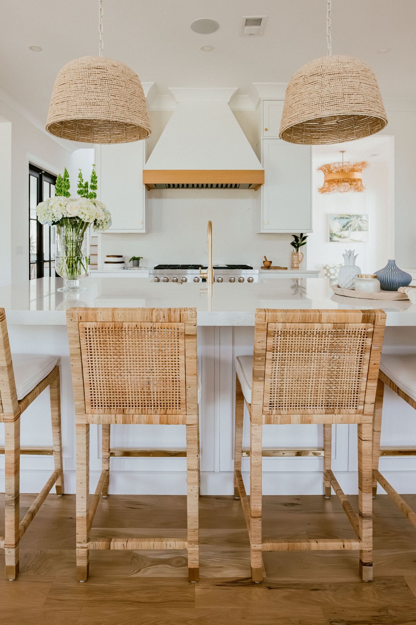 White kitchen with woven dome pendants, brass faucet, and cane counter stools