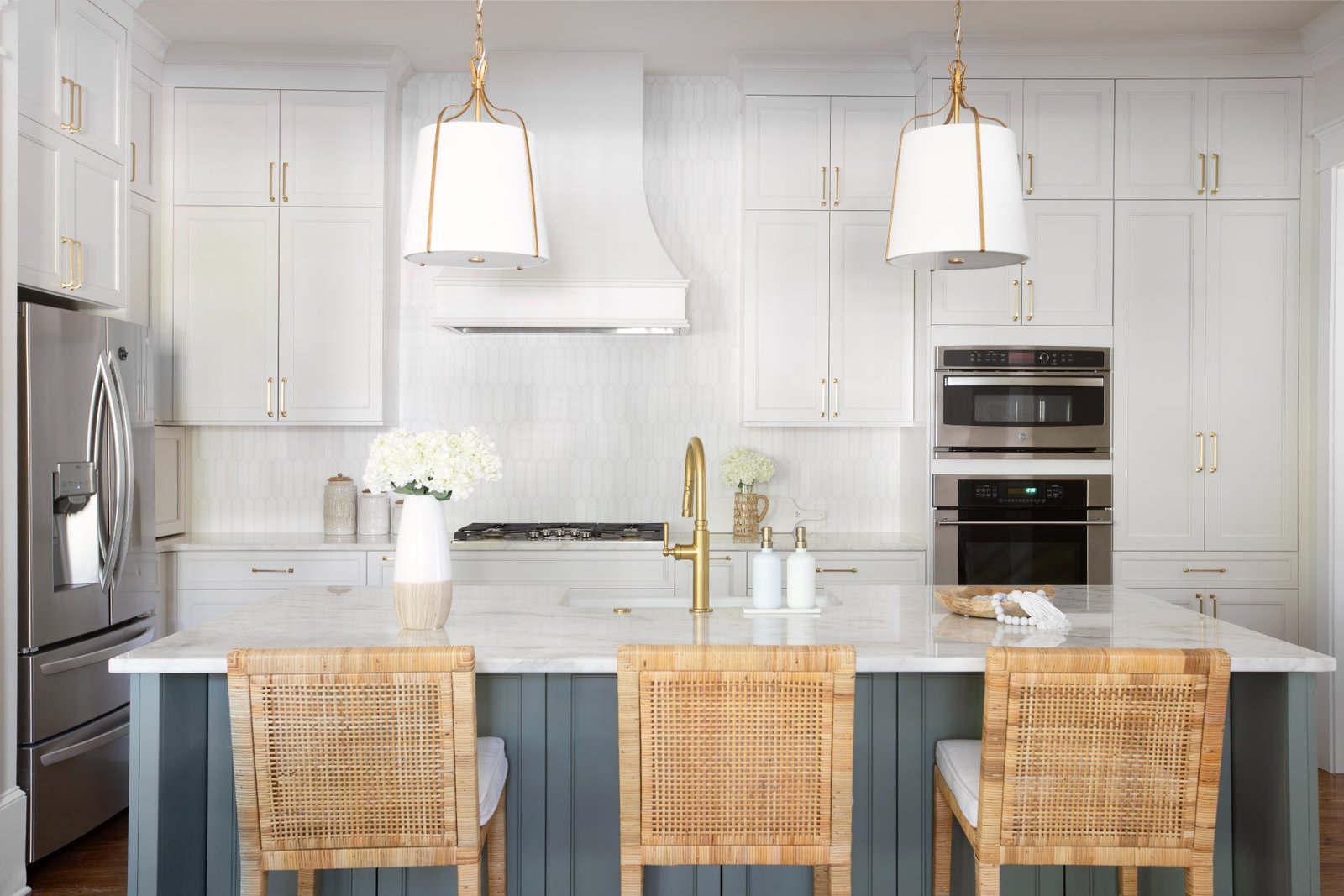 Kitchen island with cane counter stools, brass faucet, and white pendants