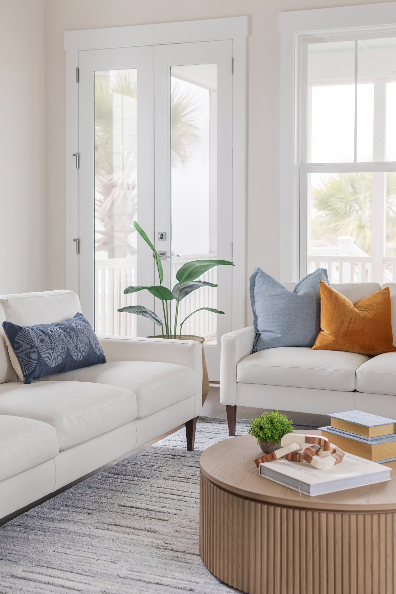 Ivory sofas with blue and amber pillows around a fluted oak coffee table by porch doors