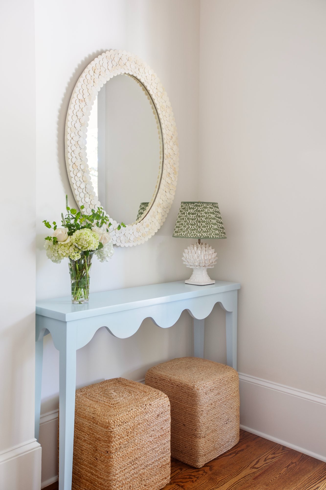 Pale blue scalloped console with capiz mirror, coral lamp, and jute stools