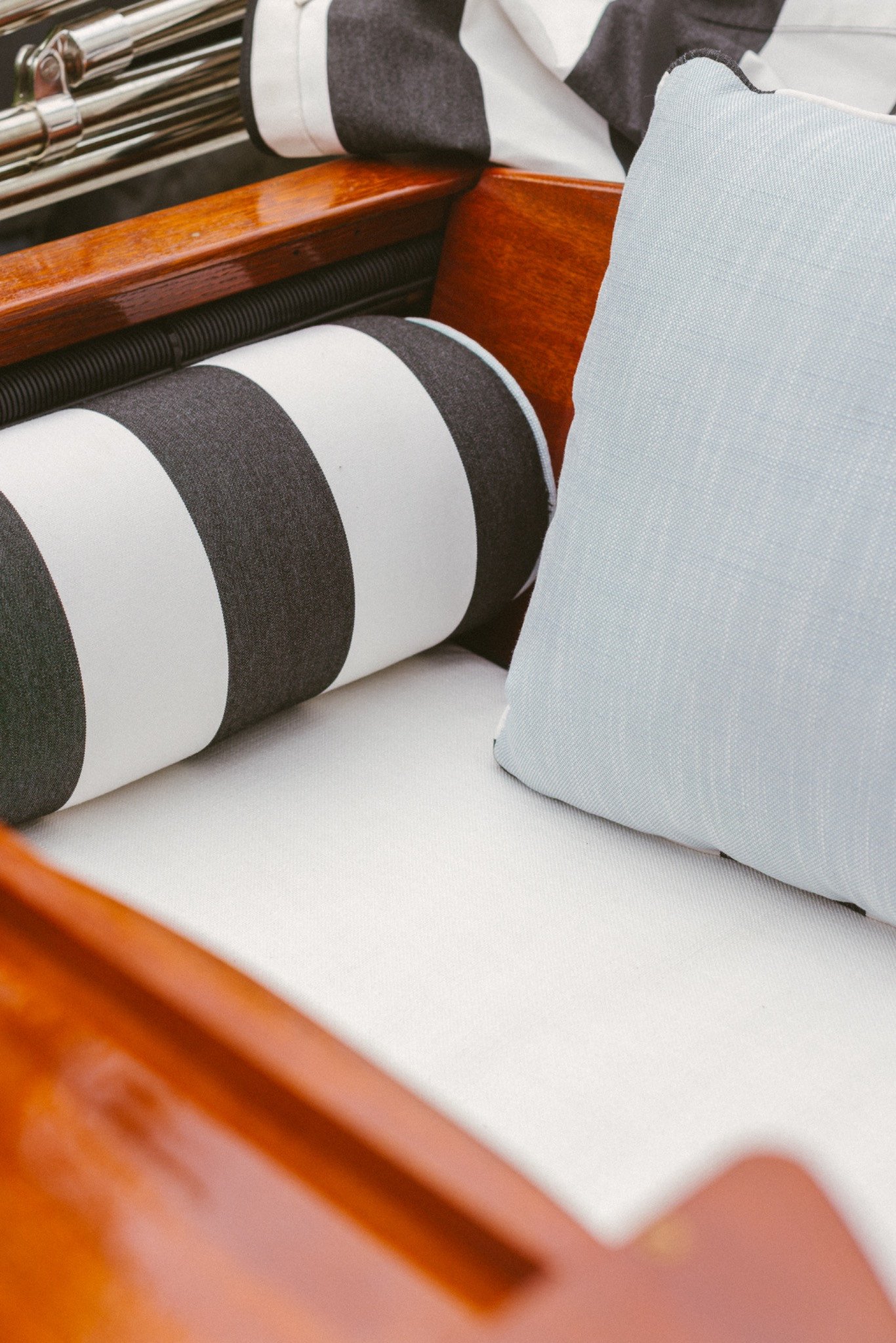 Striped bolster and pale blue linen pillow against varnished mahogany