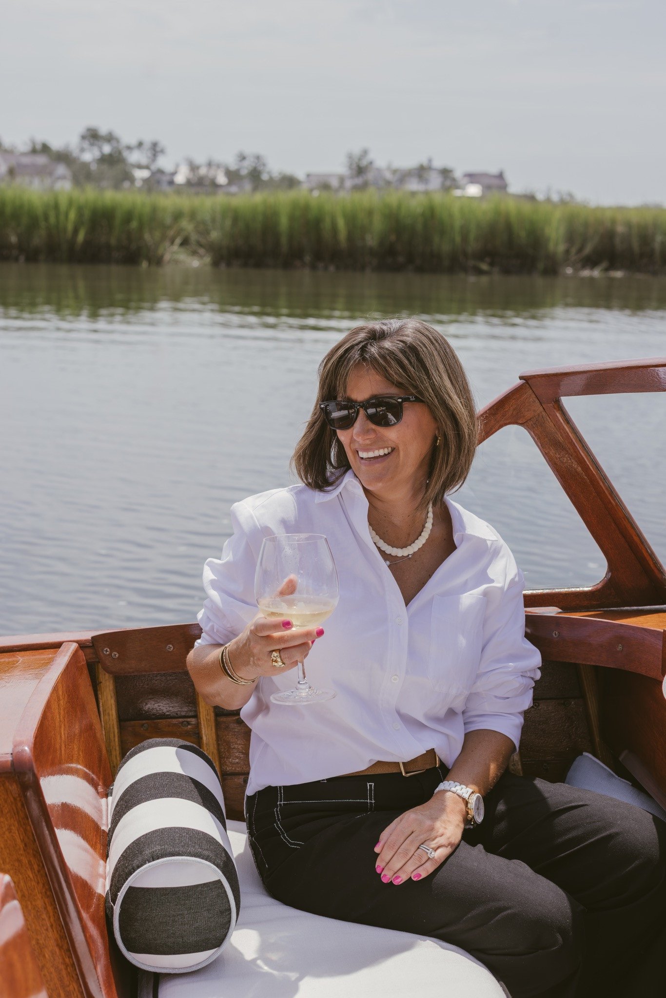A guest seated aboard with a glass of white wine, marsh grass behind