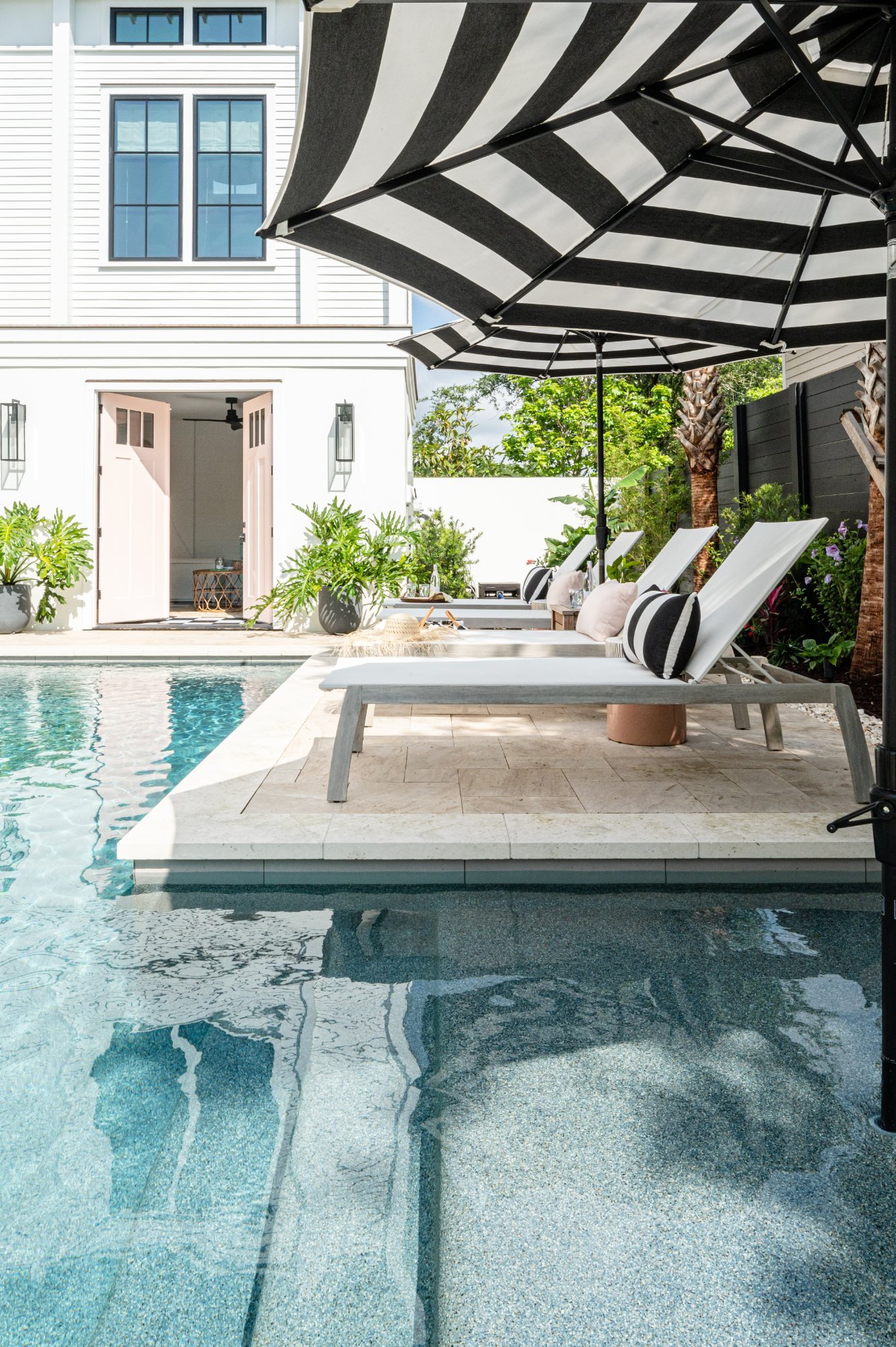 Chaises under a black-and-white striped umbrella beside the pool