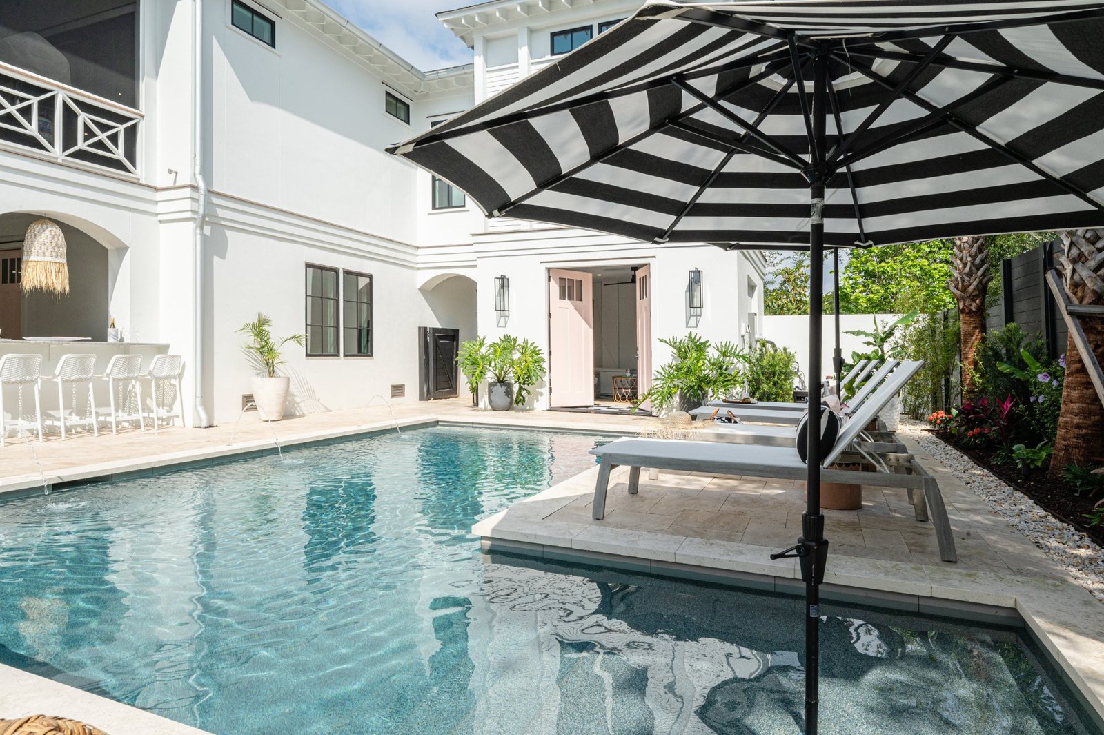 Courtyard pool with striped umbrella, chaises, and pink garden doors