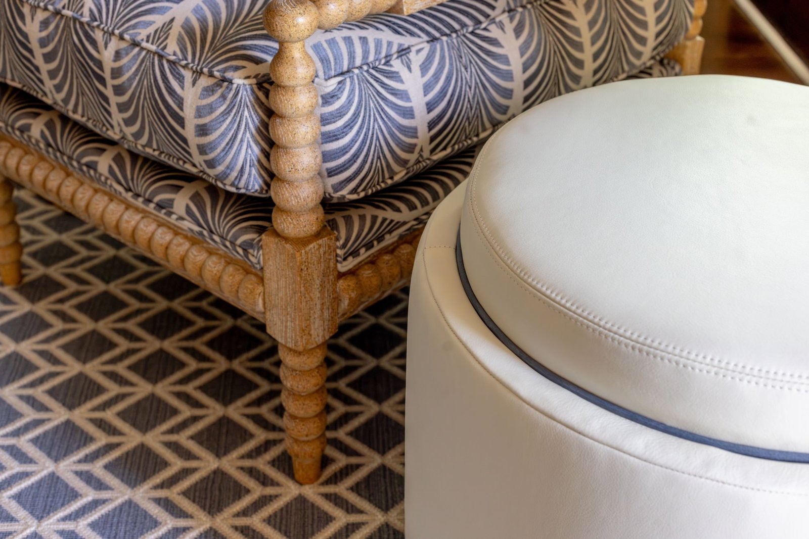 Spool-turned chair in blue palm fabric beside a white leather ottoman