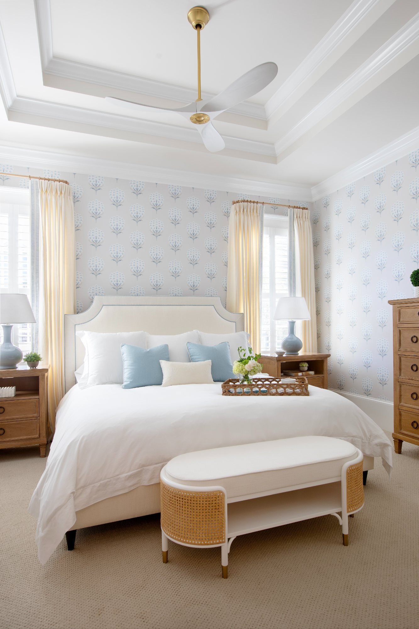 Primary bedroom with tray ceiling, block-print wallpaper, and caned bench