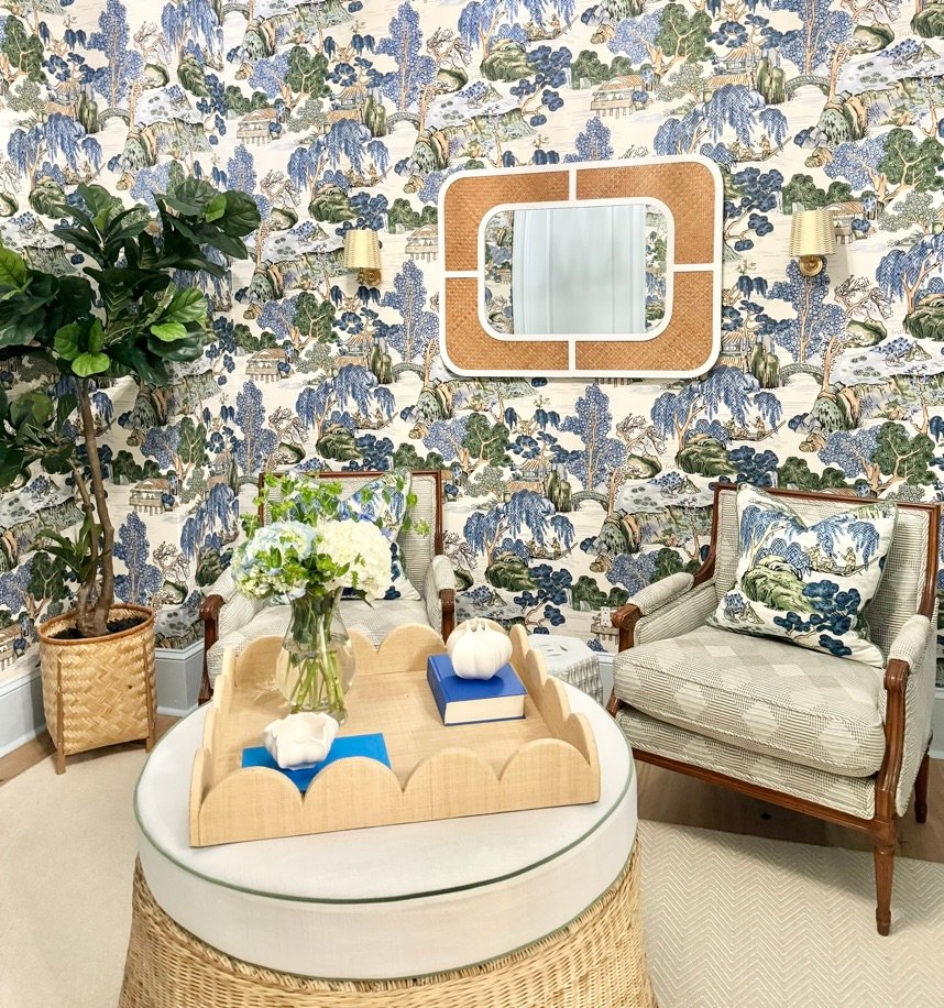 Checked armchairs and a scalloped raffia tray beneath the rattan mirror