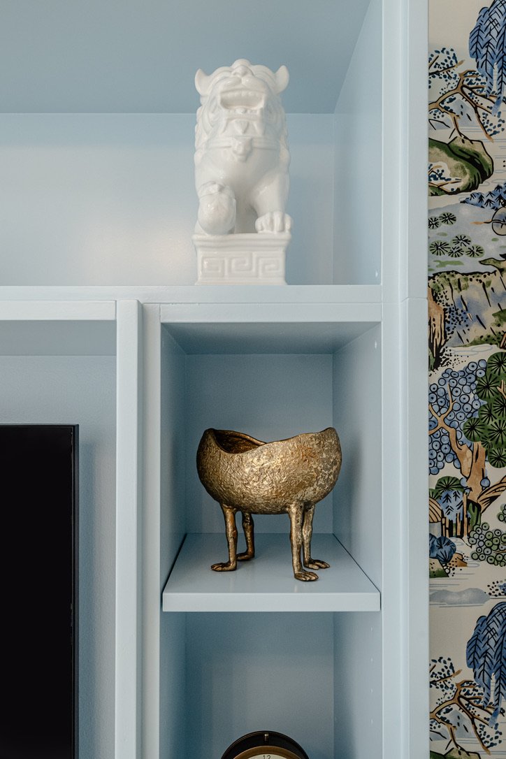 White foo dog and brass footed bowl on the pale blue built-in shelves